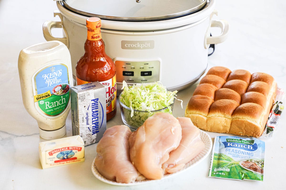 Ingredients to make Crockpot buffalo chicken sliders including chicken breasts, slider rolls, ranch, buffalo sauce, and butter.