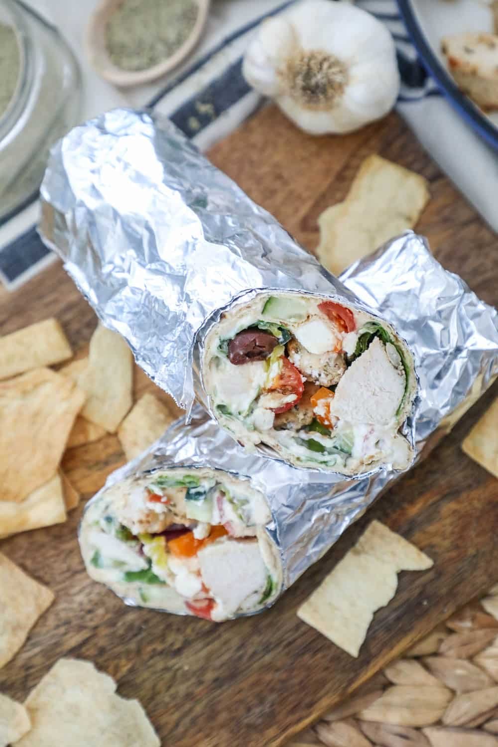 greek wrap in foil with pita chips on a wooden board