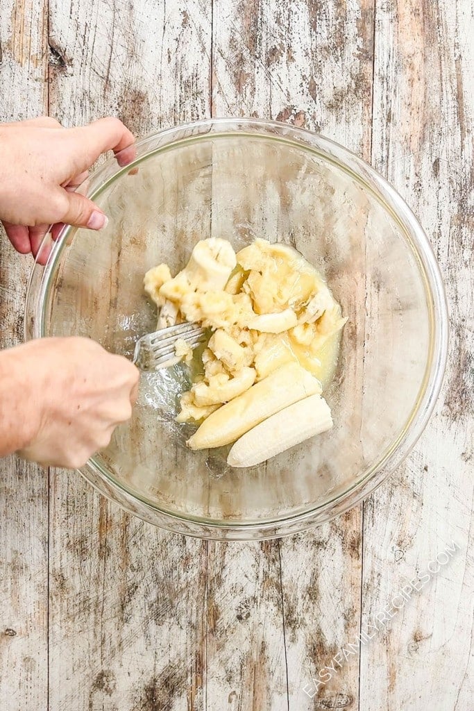 Mashing bananas in a clear glass bowl for banana bread.