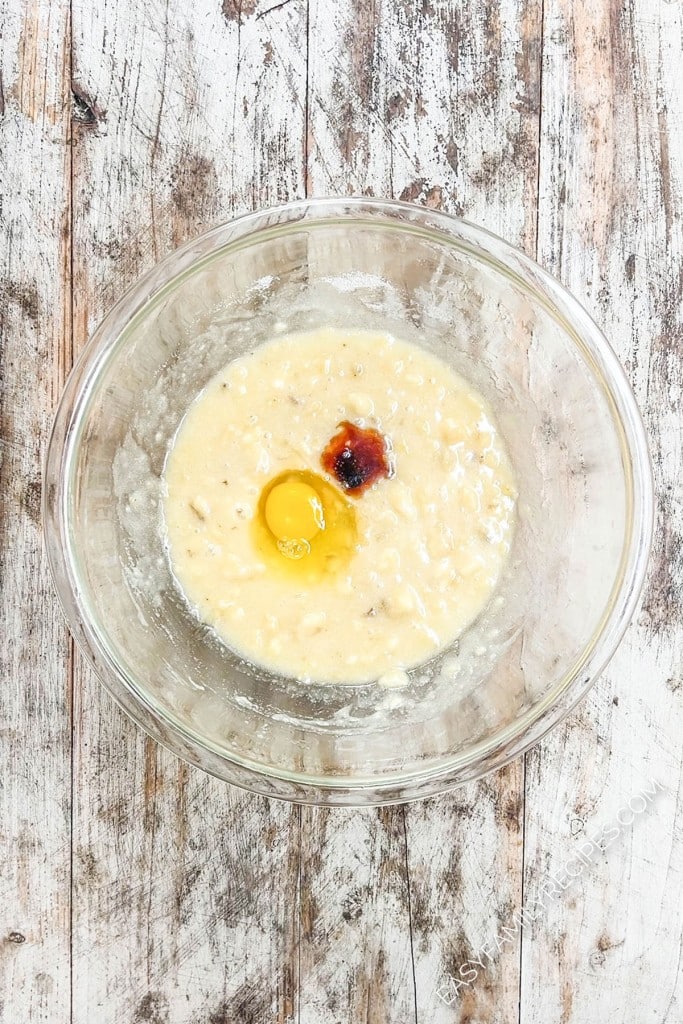 Egg and vanilla have been added to banana bread batter in a glass bowl.