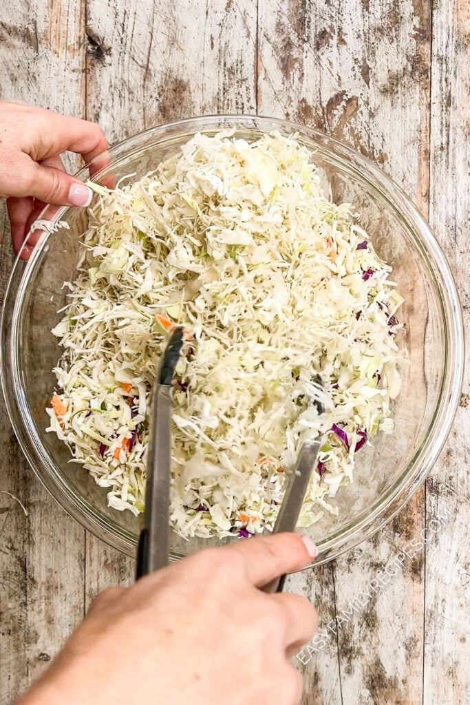 Classic southern coleslaw being mixed together with tongs.