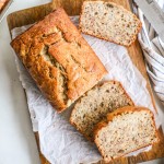 Sliced banana bread loaf on a piece of parchment paper atop a wooden board.