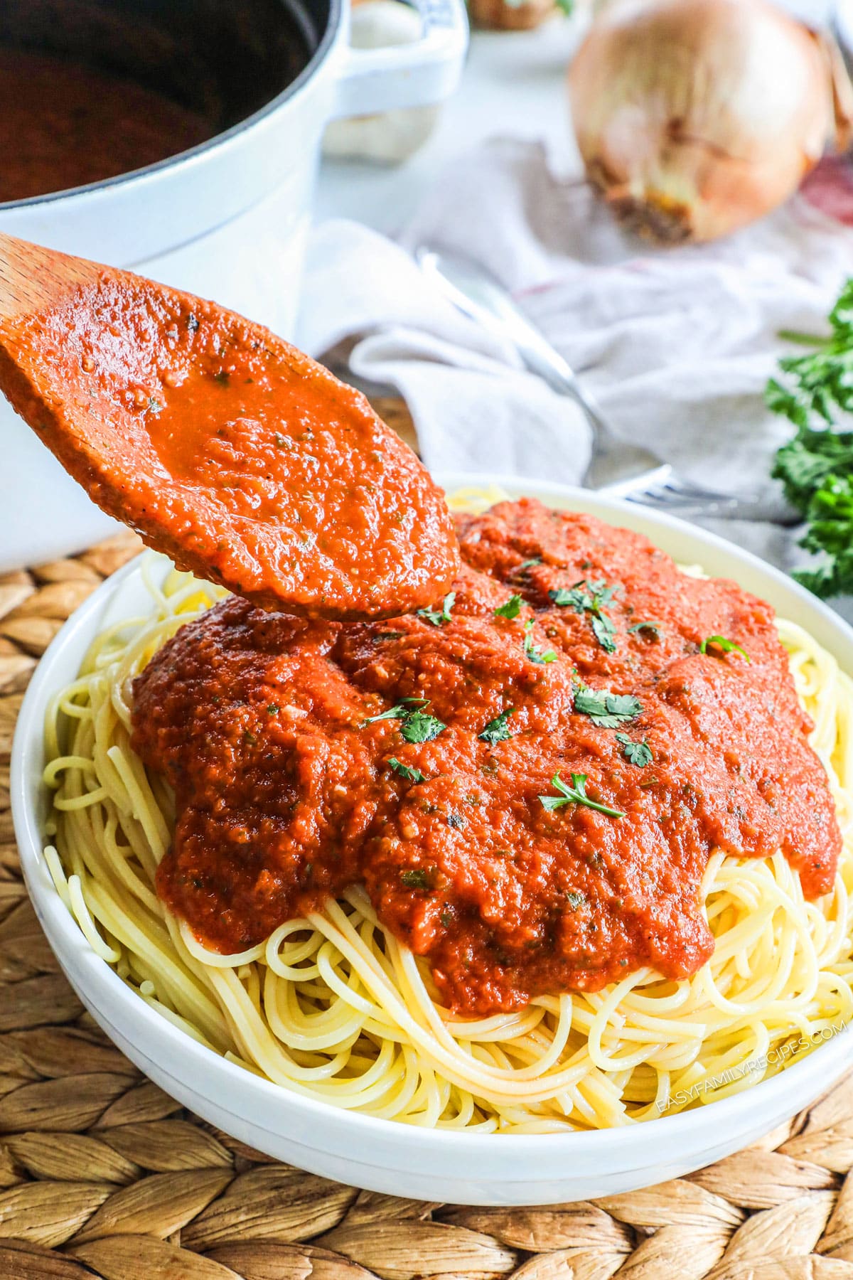 Spooning marinara sauce over spaghetti noodles