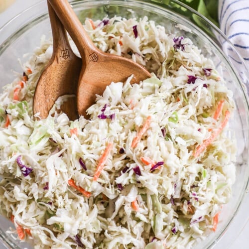 A close-up of classic Southern coleslaw salad in a glass bowl with two wooden spoons.