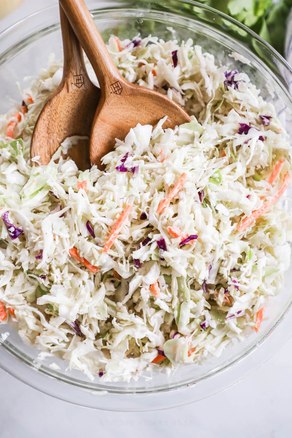 A close-up of classic Southern coleslaw salad in a glass bowl with two wooden spoons. 