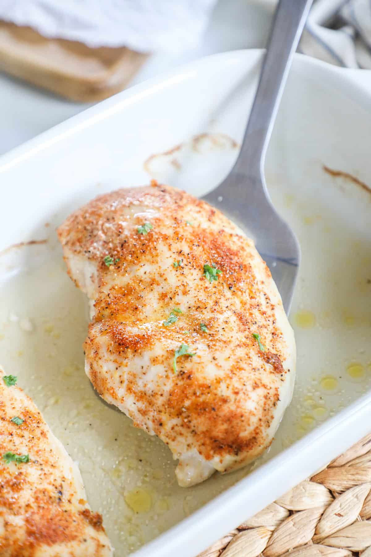 baked chicken being taking out of a white dish with a spatula 