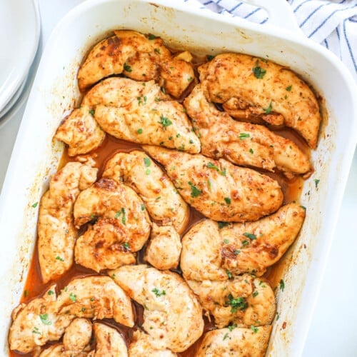 Oven baked chicken tenders with no breading in a white casserole dish, ready to serve