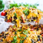 Chicken breast topped with beans, red pepper, corn and cheese being lifted out of the baking dish to serve for an easy dinner.