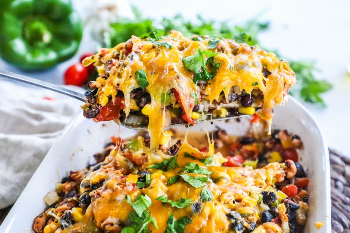 Chicken breast topped with beans, red pepper, corn and cheese being lifted out of the baking dish to serve for an easy dinner.