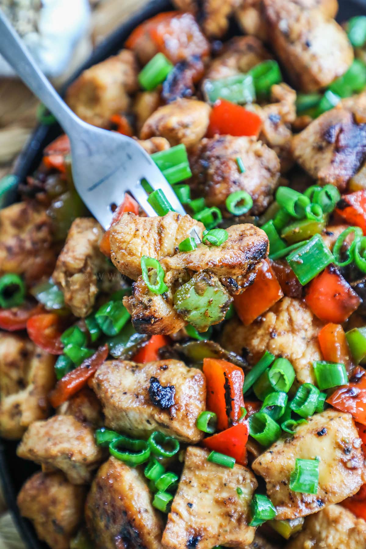 cajun chicken skillet with a spoon scooping chicken out chicken and peppers. 