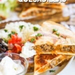 two slices of ground beef quesadilla stacked on a plate with rice, black bean, sour cream, and tomato.