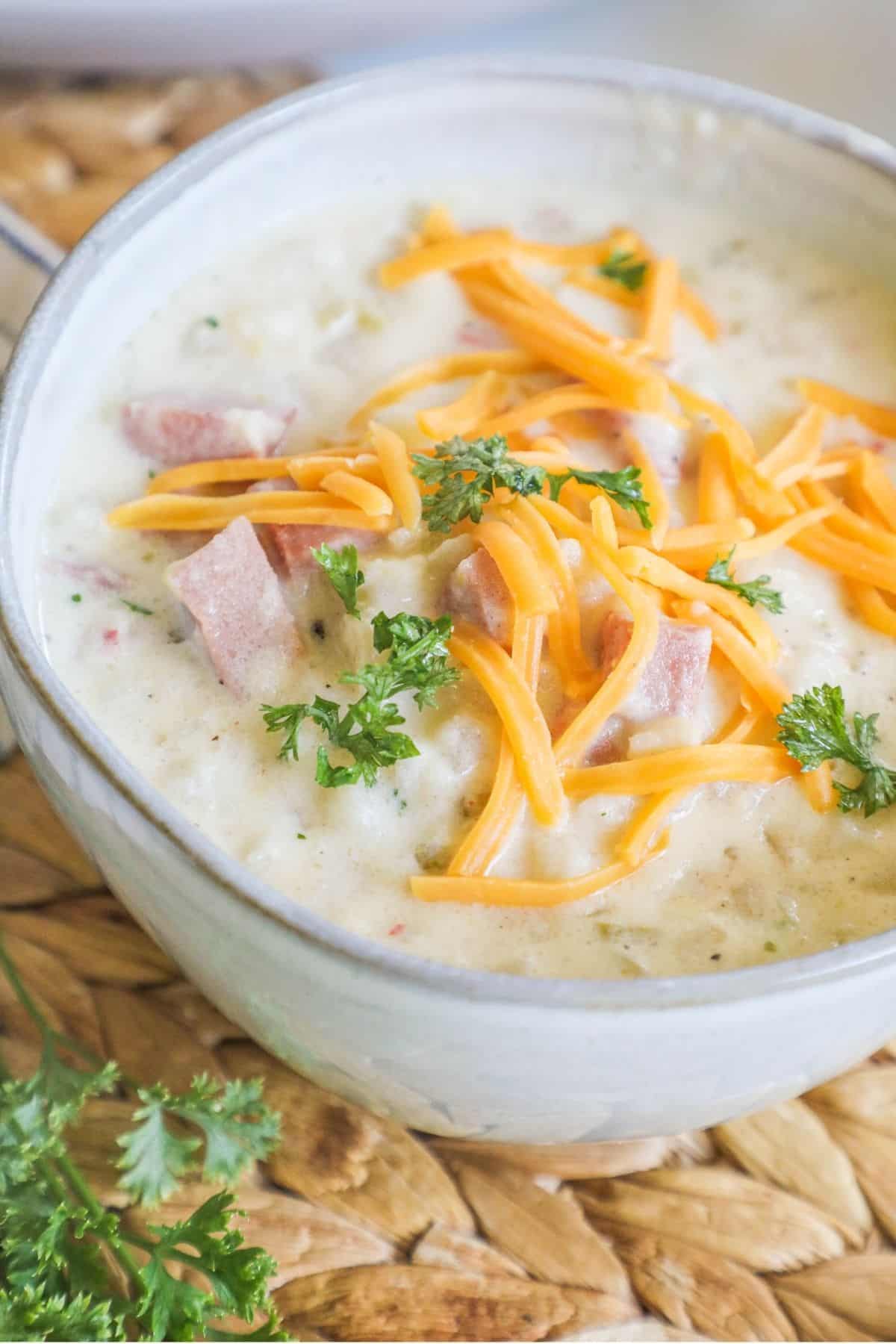 ham and potato soup in a white bowl topped with cheese
