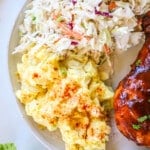 Potato salad with eggs on a plate with coleslaw and bbq'd meat.