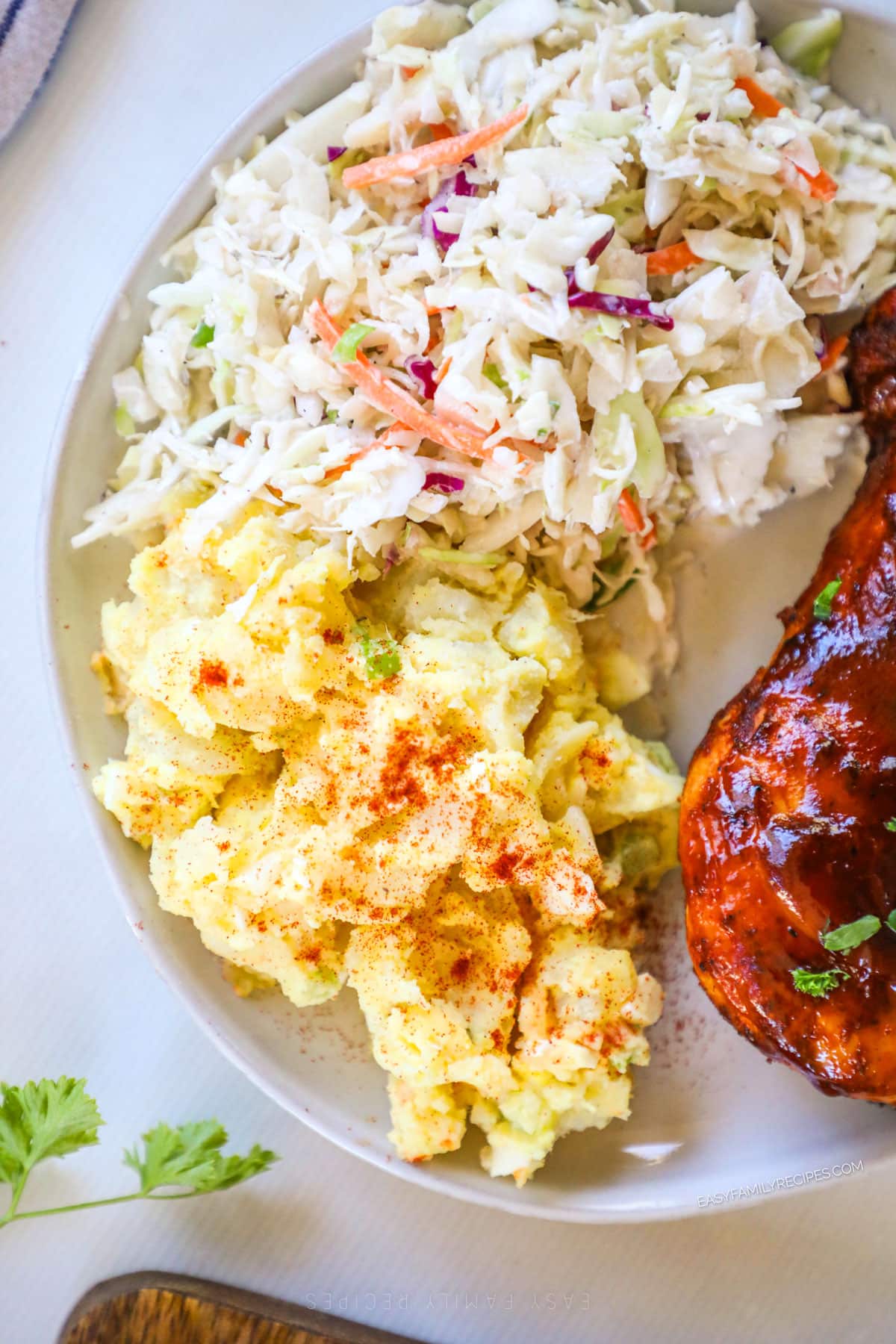Potato salad with eggs on a plate with coleslaw and bbq'd meat.
