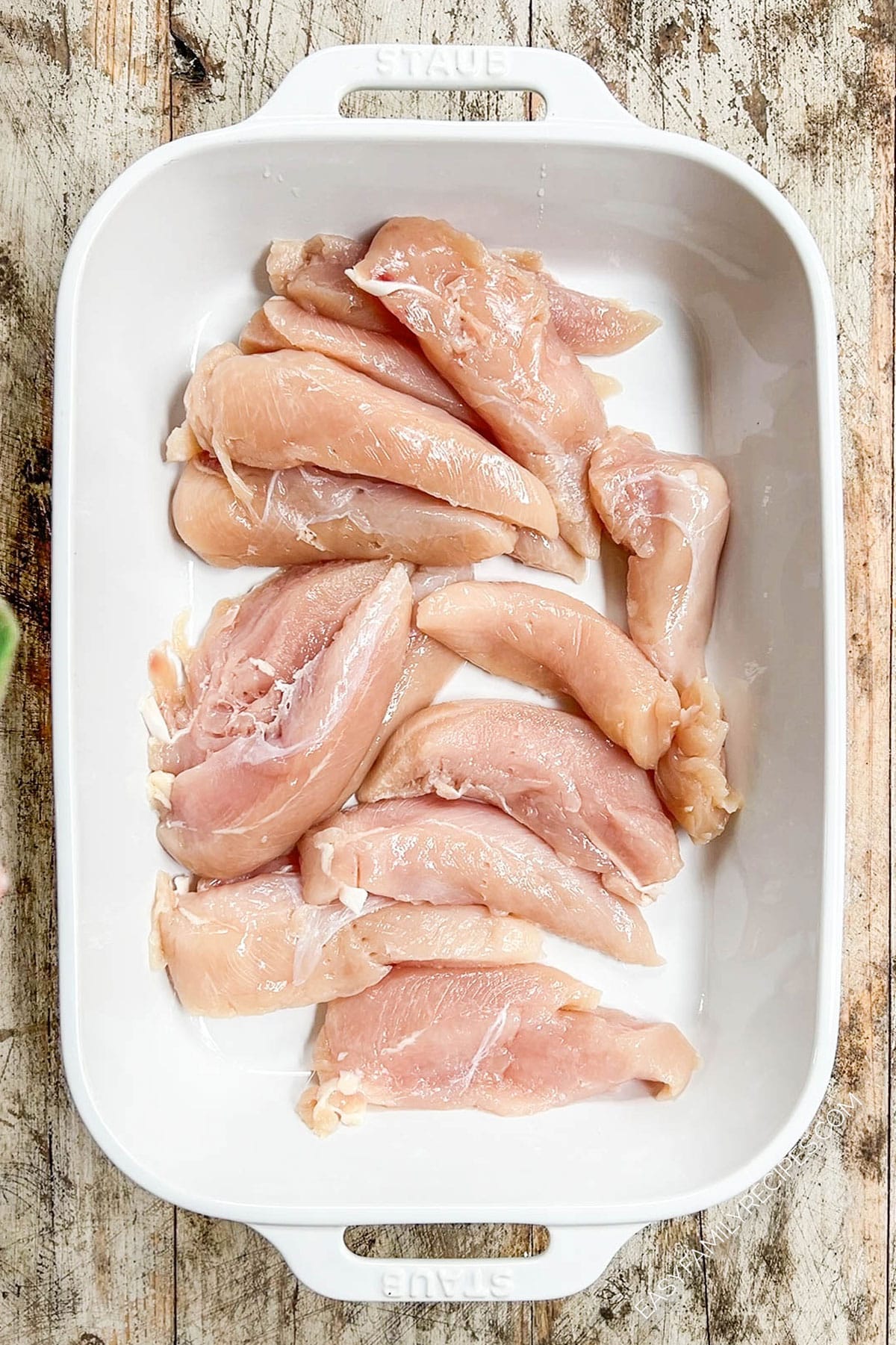 Chicken for oven-baked tenders is placed in a casserole dish.