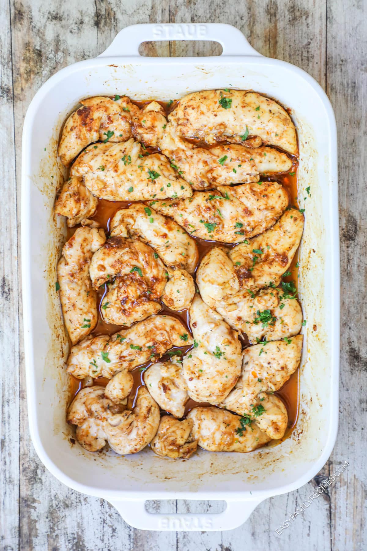 A white casserole dish full of Oven baked chicken tenders with no breading.