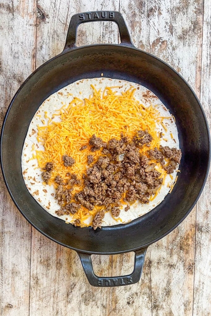 beef and cheese being cooked on a tortilla.