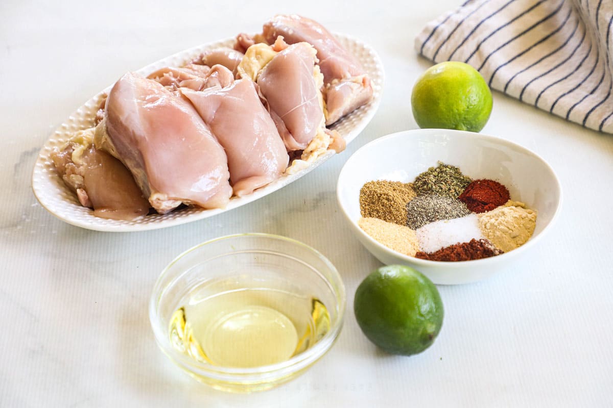 Ingredients for Mexican Chicken thighs including spices, lime, oil, and boneless, skinless chicken thighs.