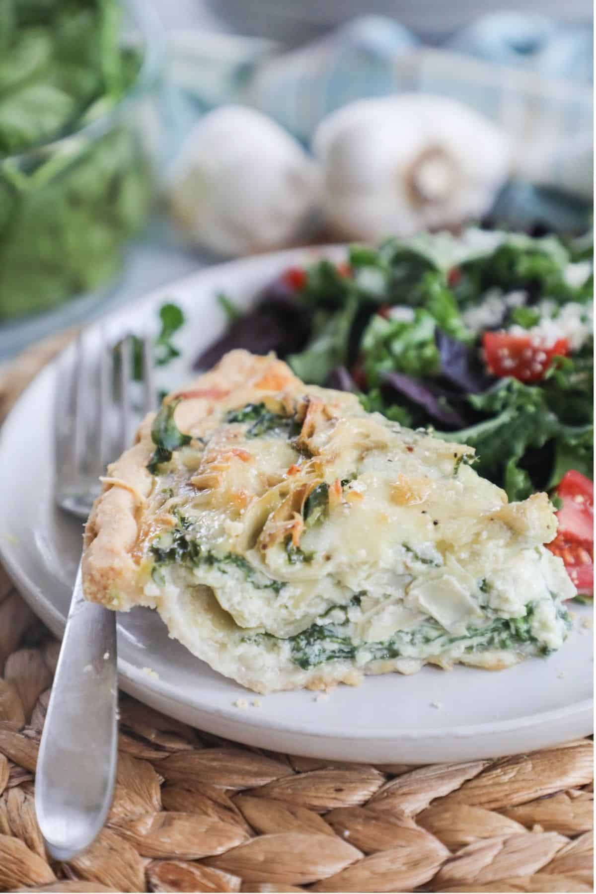 slice of spinach artichoke quiche on a plate with a side salad