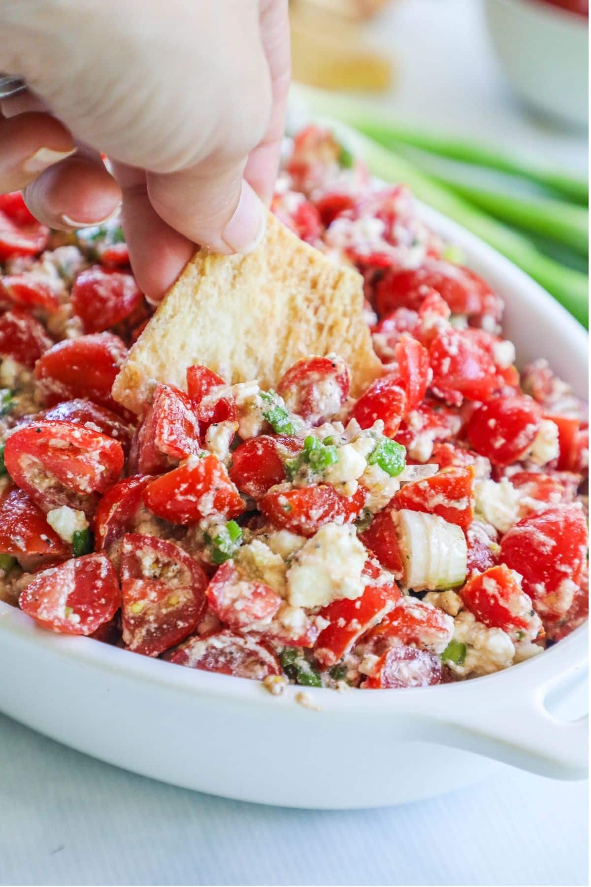 a pita chip being dipped into a bowl of tomato feta dip