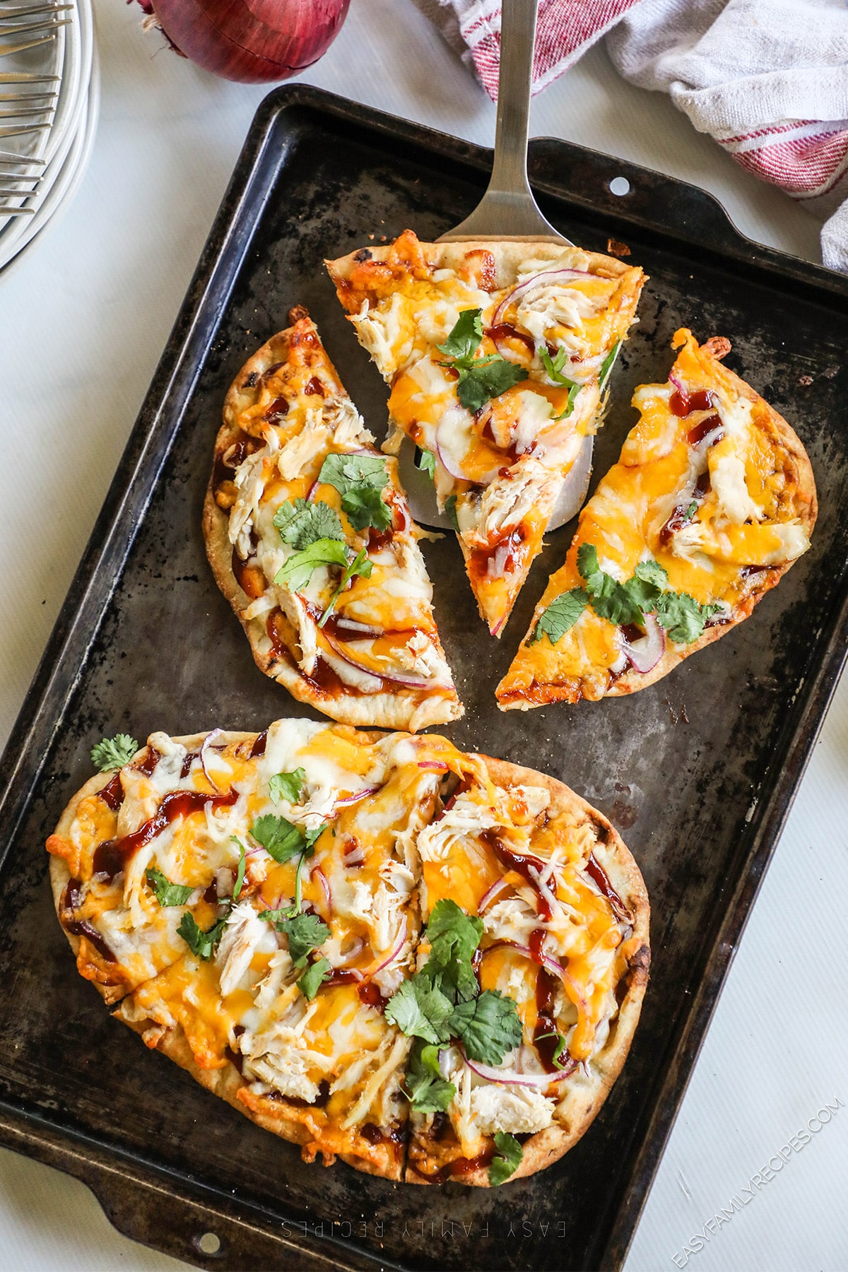 two flatbread pizzas on a baking sheet with one cut into slices.