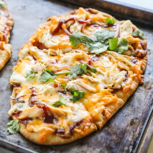 above image of a whole bbq chicken flatbread naan pizza on a baking sheet.
