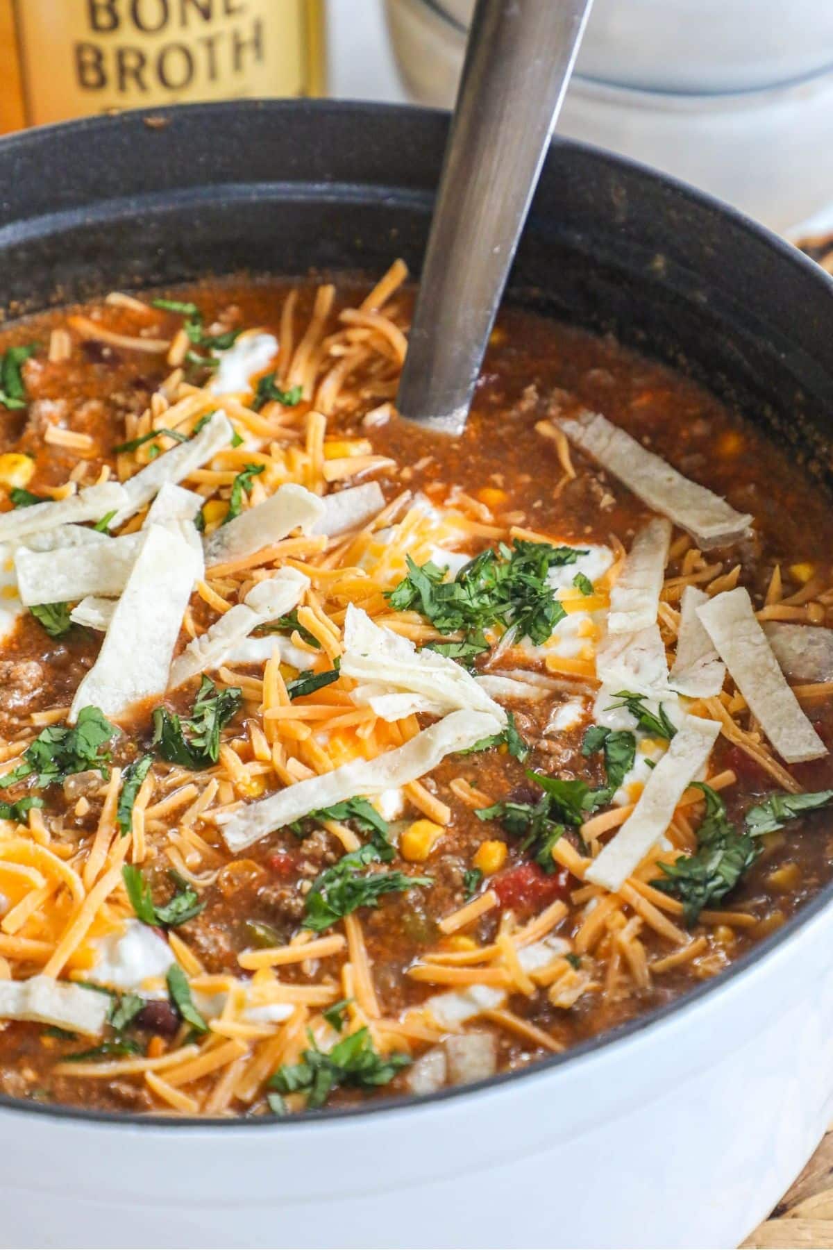 beef enchilada soup topped with cheese and tortilla strips in a white pot