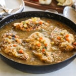 Rustic braised chicken in pan with sauce and veggies.