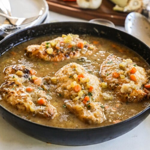 Rustic braised chicken in pan with sauce and veggies.