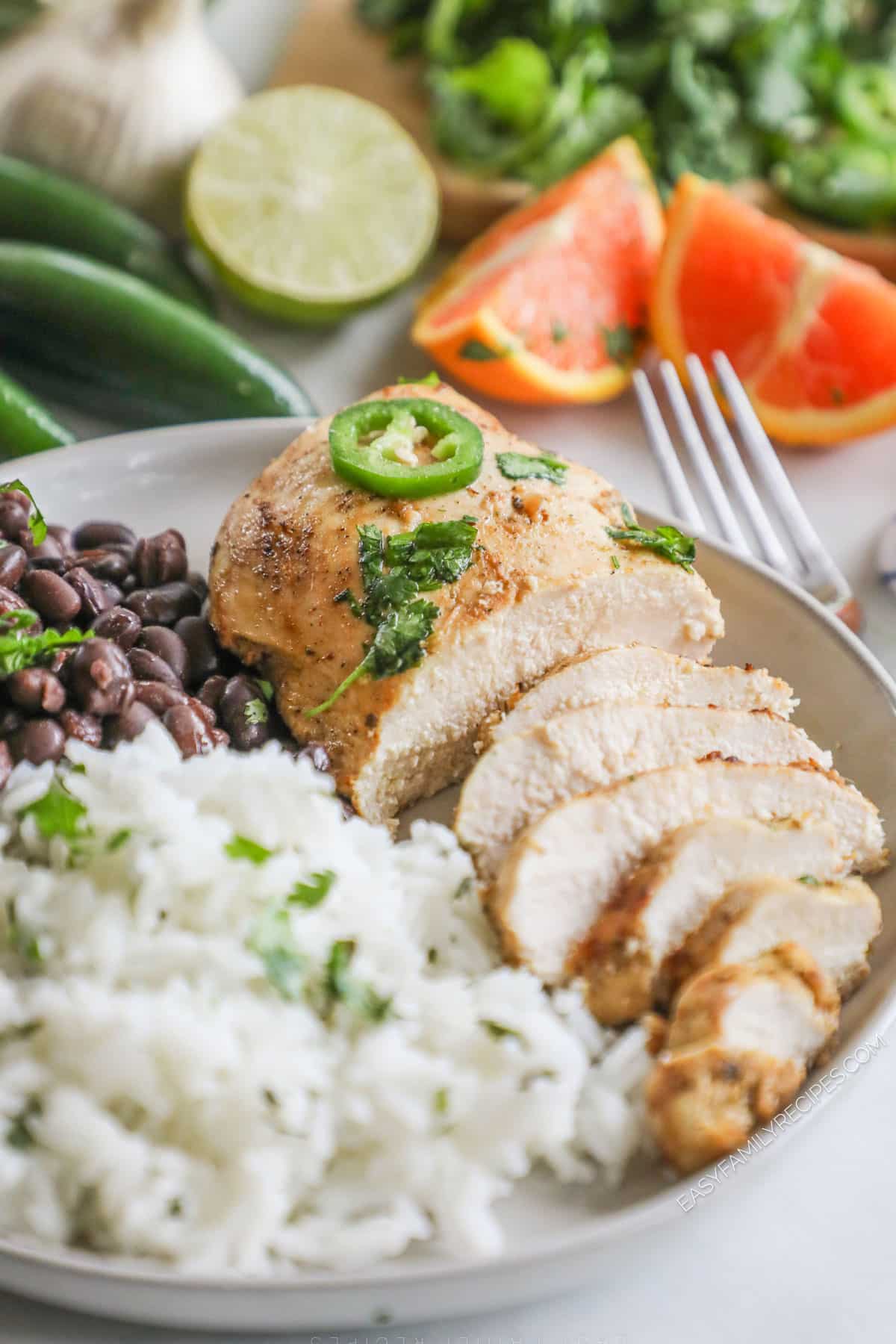 Baja Chicken sliced on a plate with rice and beans. Citrus is in the background.