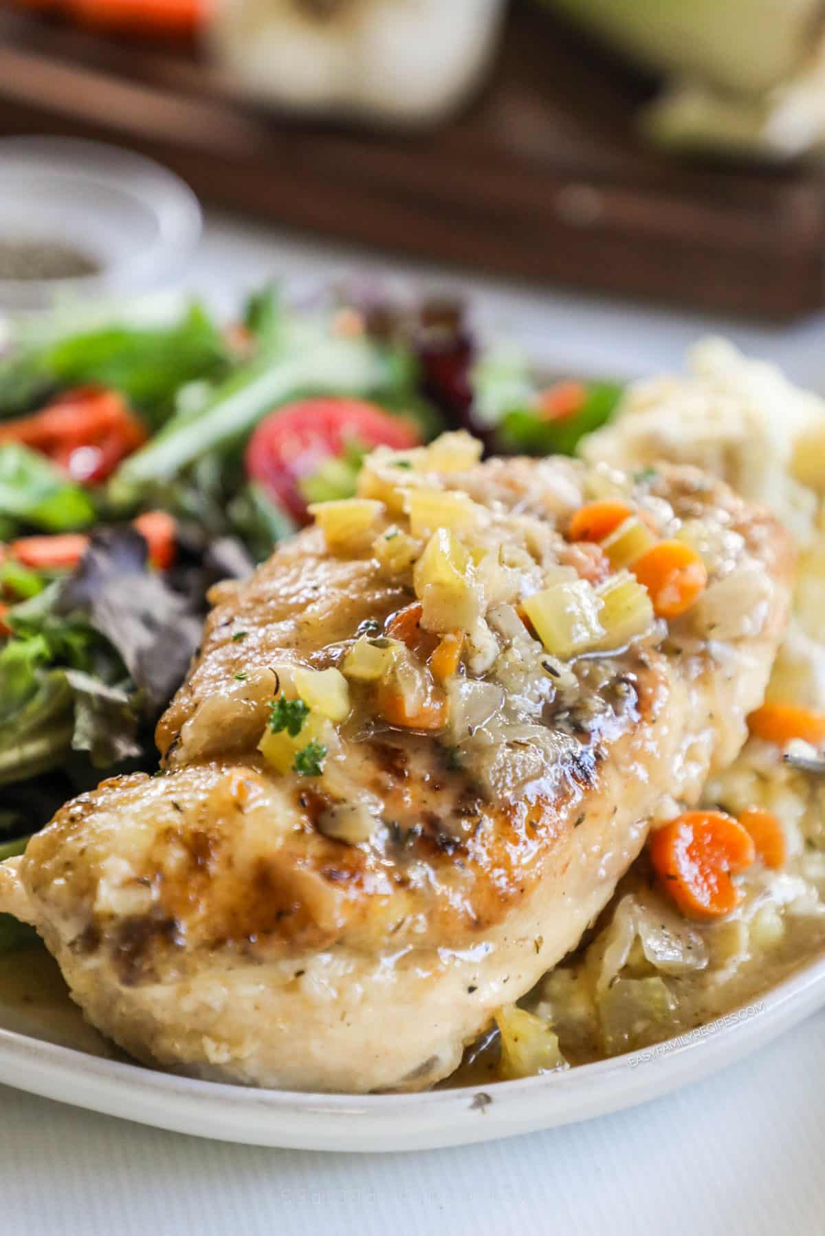 Close up of a serving of braised chicken breast on a plate with a spring salad.