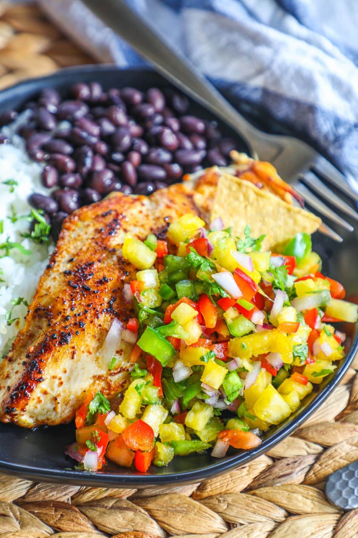 grilled chicken breast topped with pineapple salsa on a plate with rice and black beans