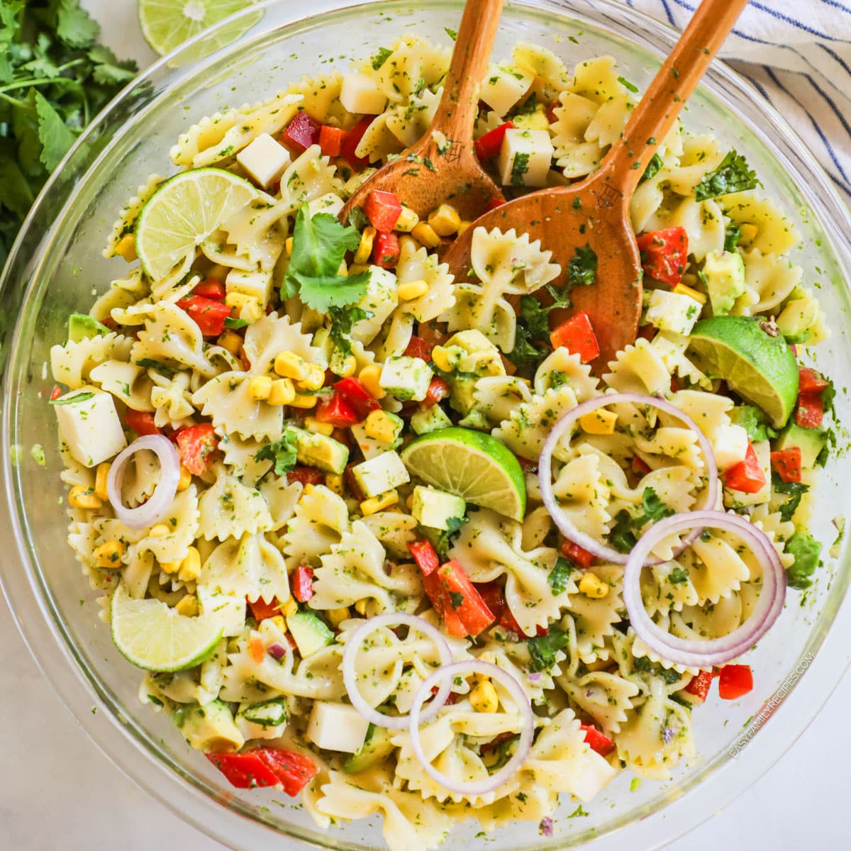 a large bowl of cilantro lime pasta salad with two wooden spoons ready to serve.