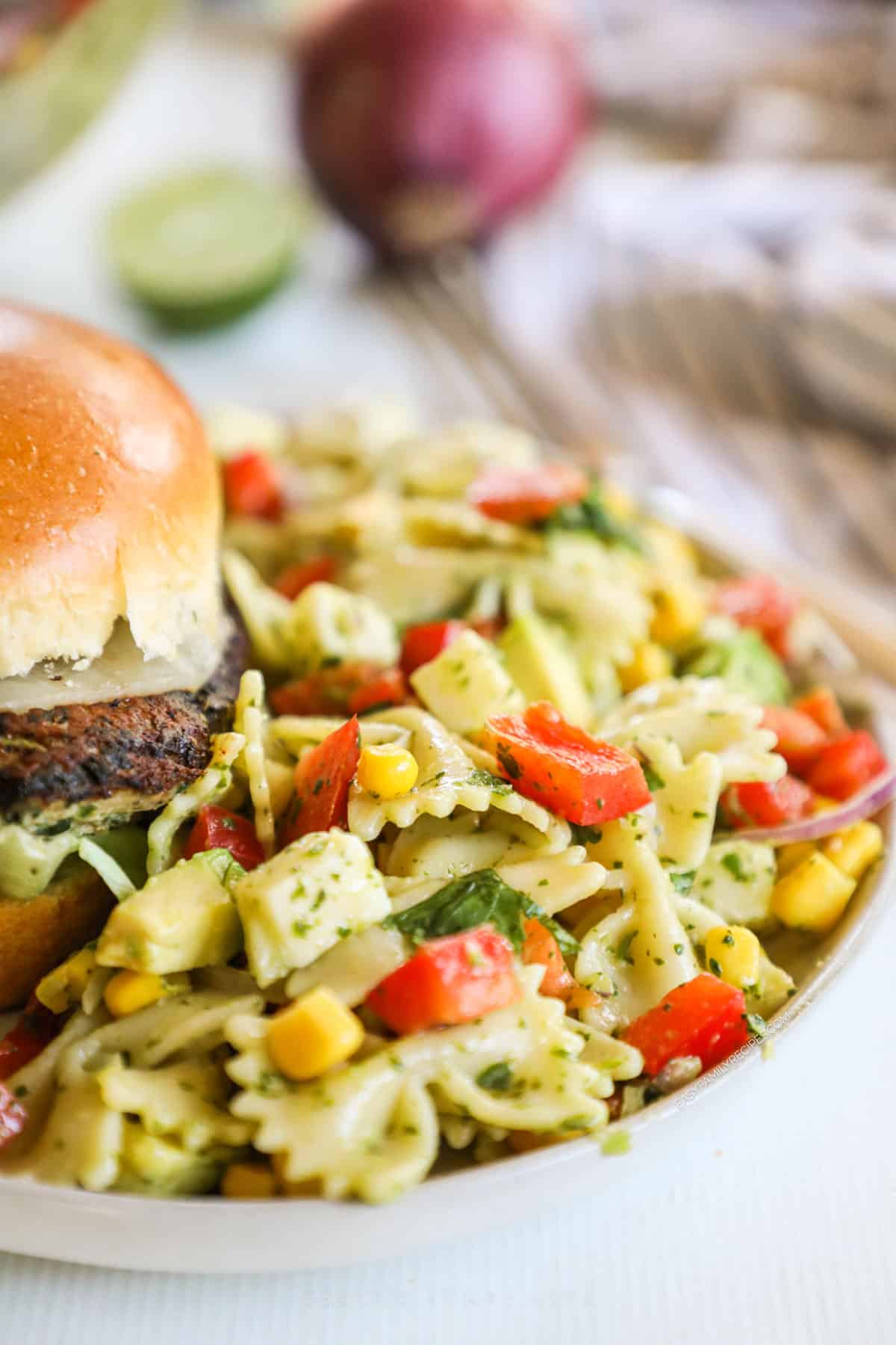 a plate with a lot of cilantro lime pasta salad beside a burger.