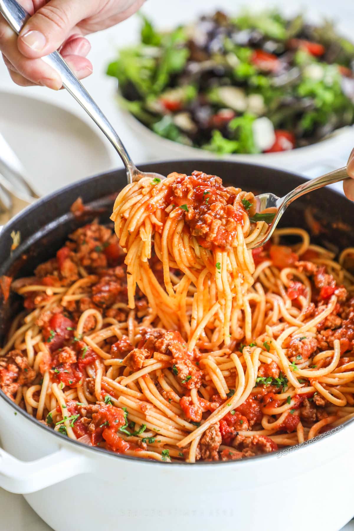 Ground turkey spaghetti in a pot with utensils lifting some up.