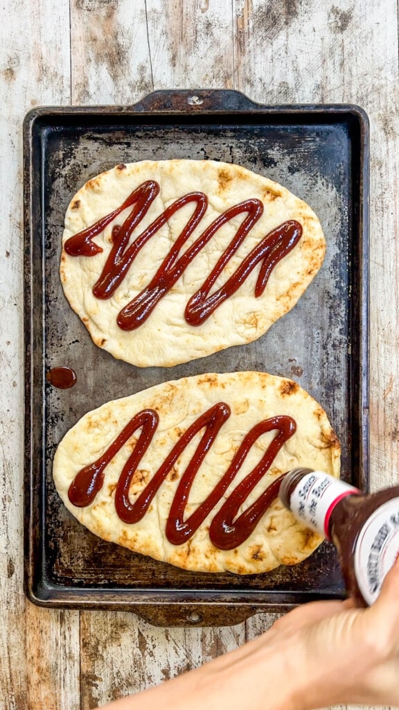 bbq sauce being drizzled on two flatbreads.