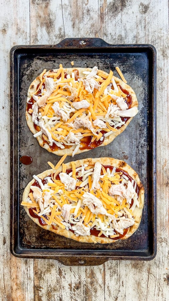 two unbaked flatbread pizzas on a baking sheet.