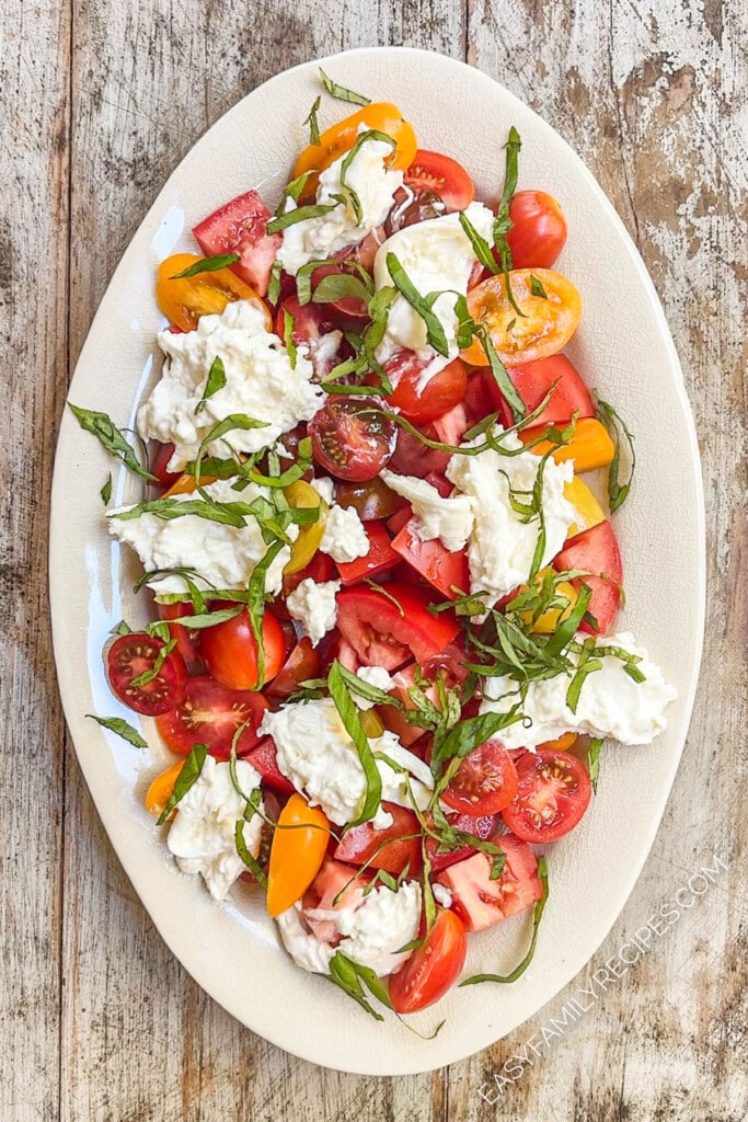 fresh tomatoes topped with burrata cheese and basil on a platter.