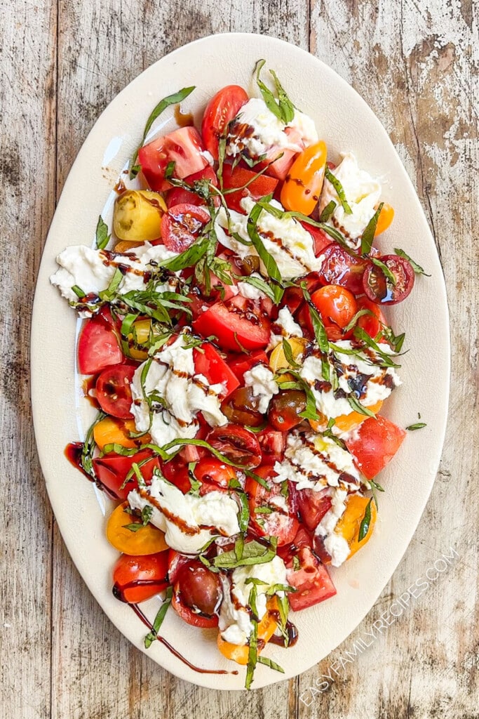 above image of an assembled burrata caprese salad drizzled with balsamic glaze.