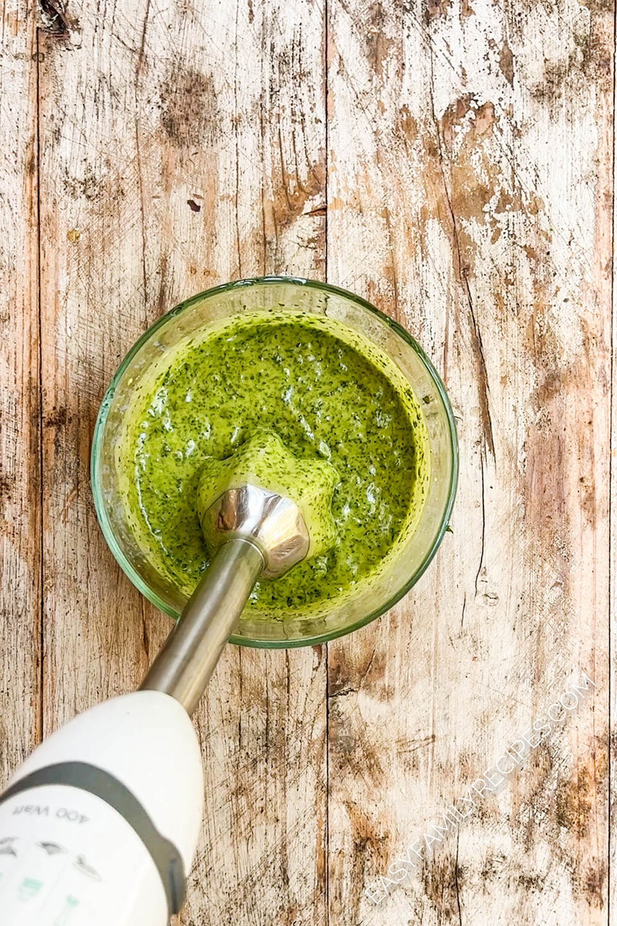 An immersion blender in a bowl with a green, creamy dressing.