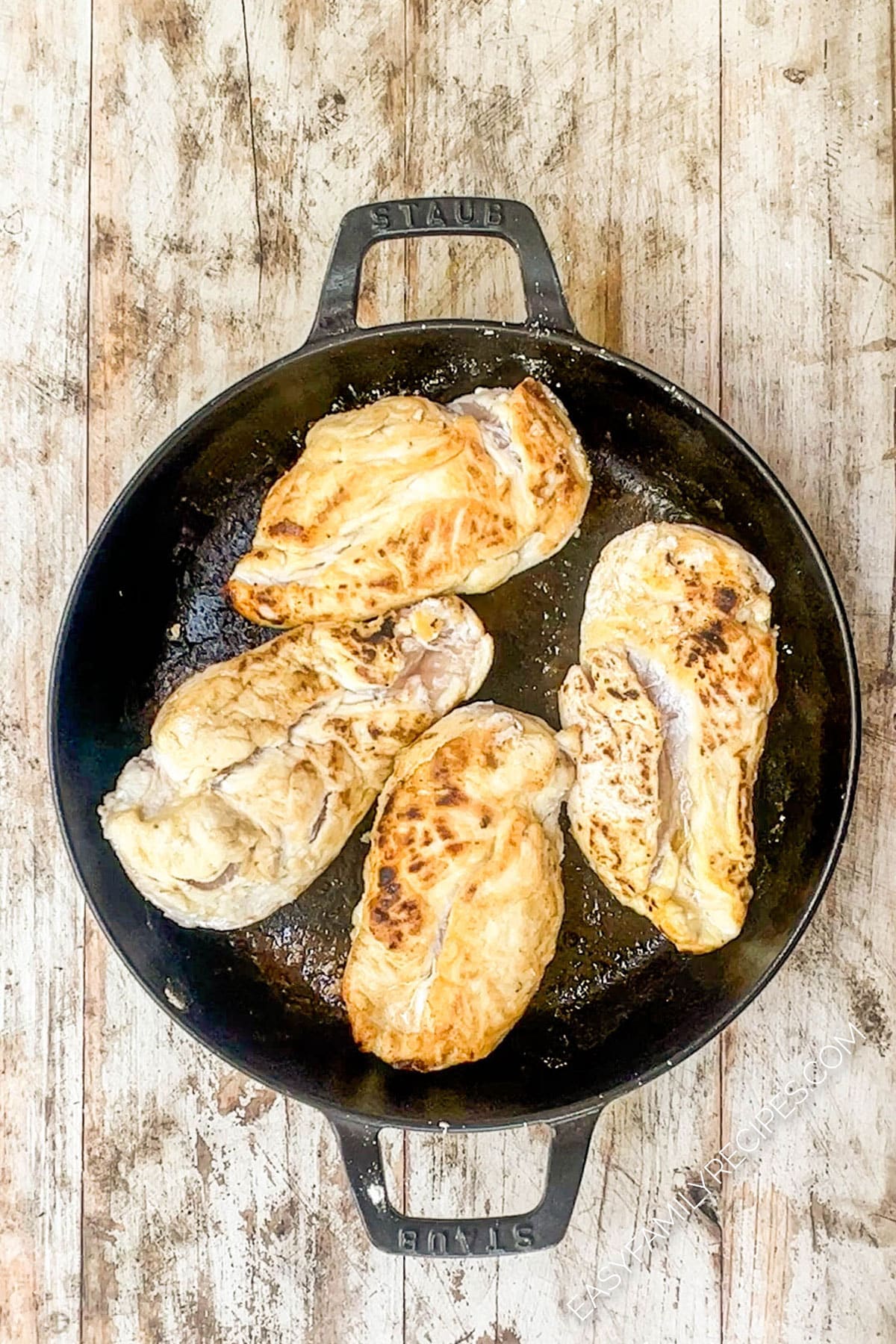 Four chicken breasts in a pan after searing.