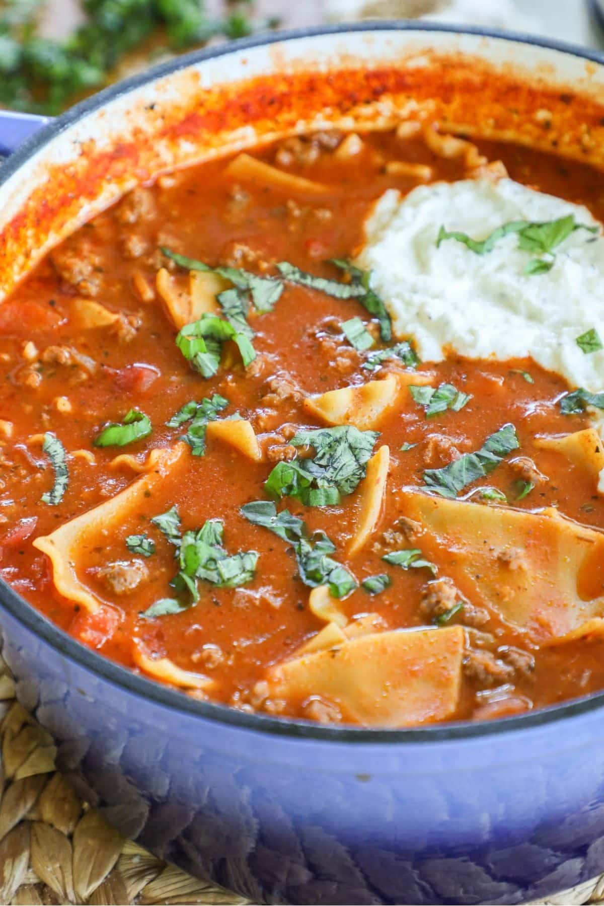 lasagna soup topped with basil and a scoop of ricotta cheese in a blue pot