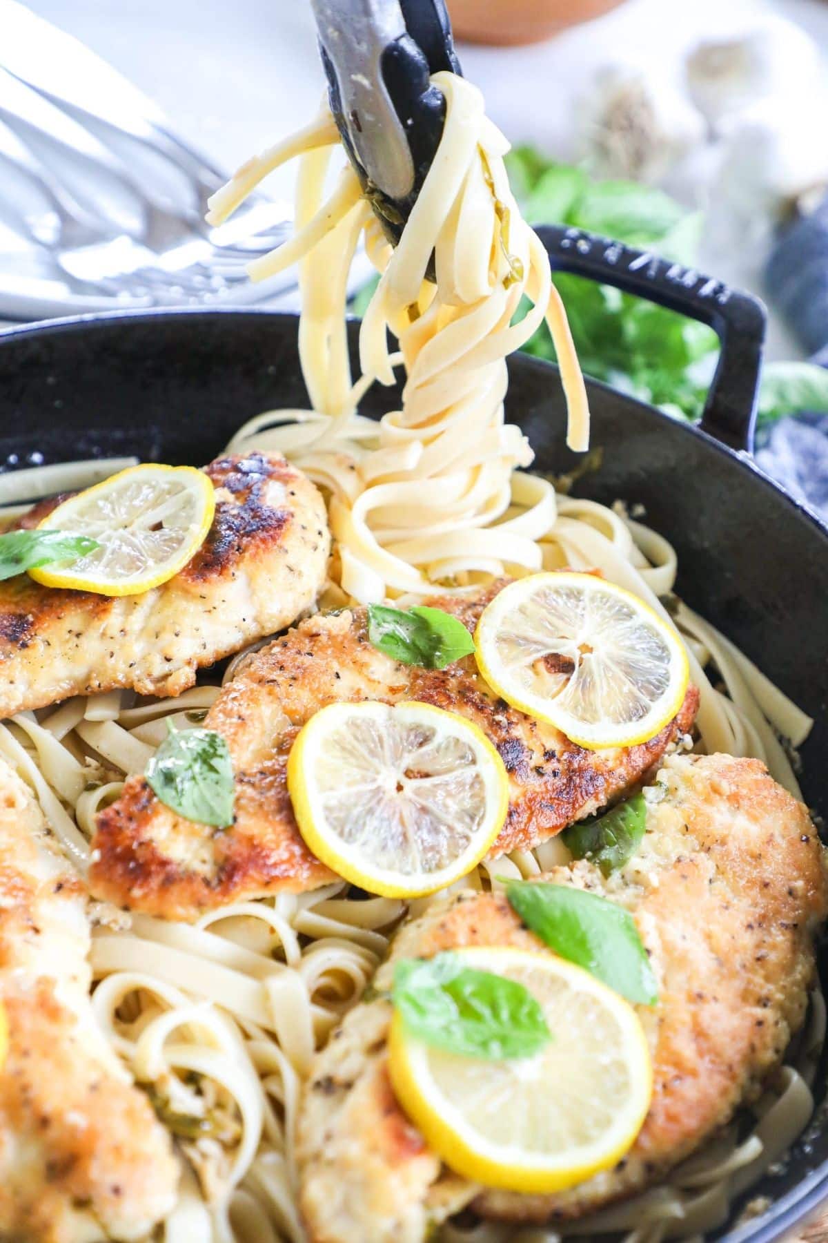 lemon basil pasta topped with chicken cutlets and lemon slices in a skillet