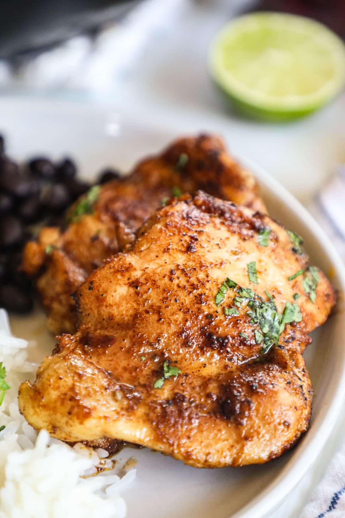 mexican seasoned chicken thighs on a plate with white rice and black beans