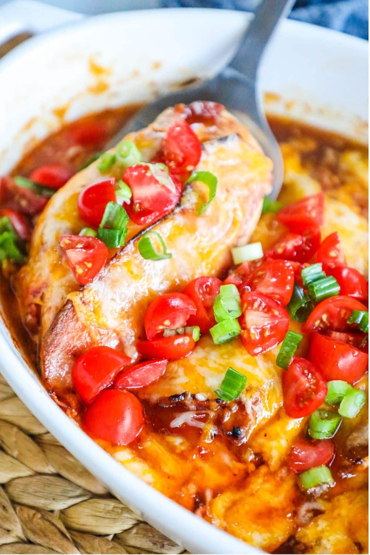 baked chicken breast in a casserole dish topped with cheese, tomatoes, and green onions