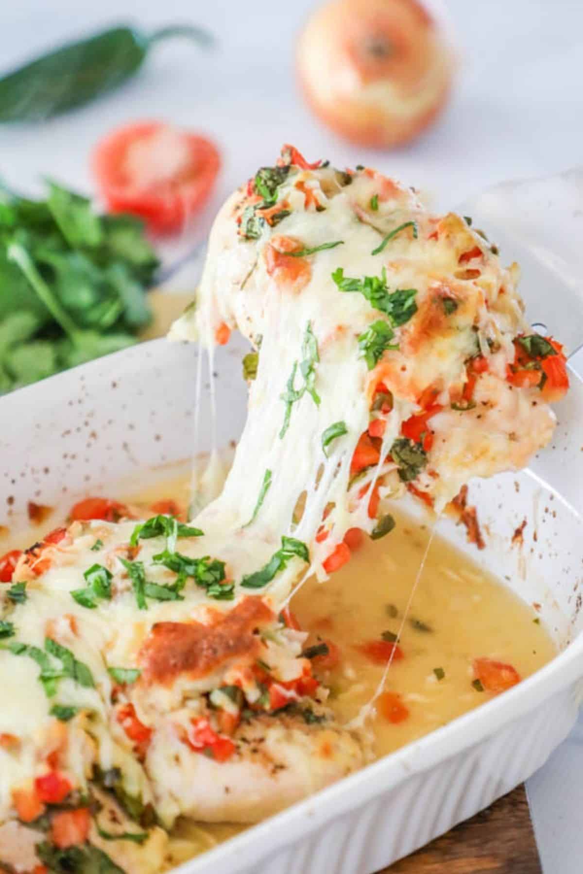 chicken breast topped with tomato and cheese in a white baking dish