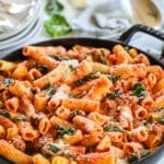 A large black pan full of creamy Tuscan sausage pasta with wilted spinach.