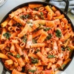 a large black cast iron pan full of creamy Italian sausage pasta in a tomato sauce.