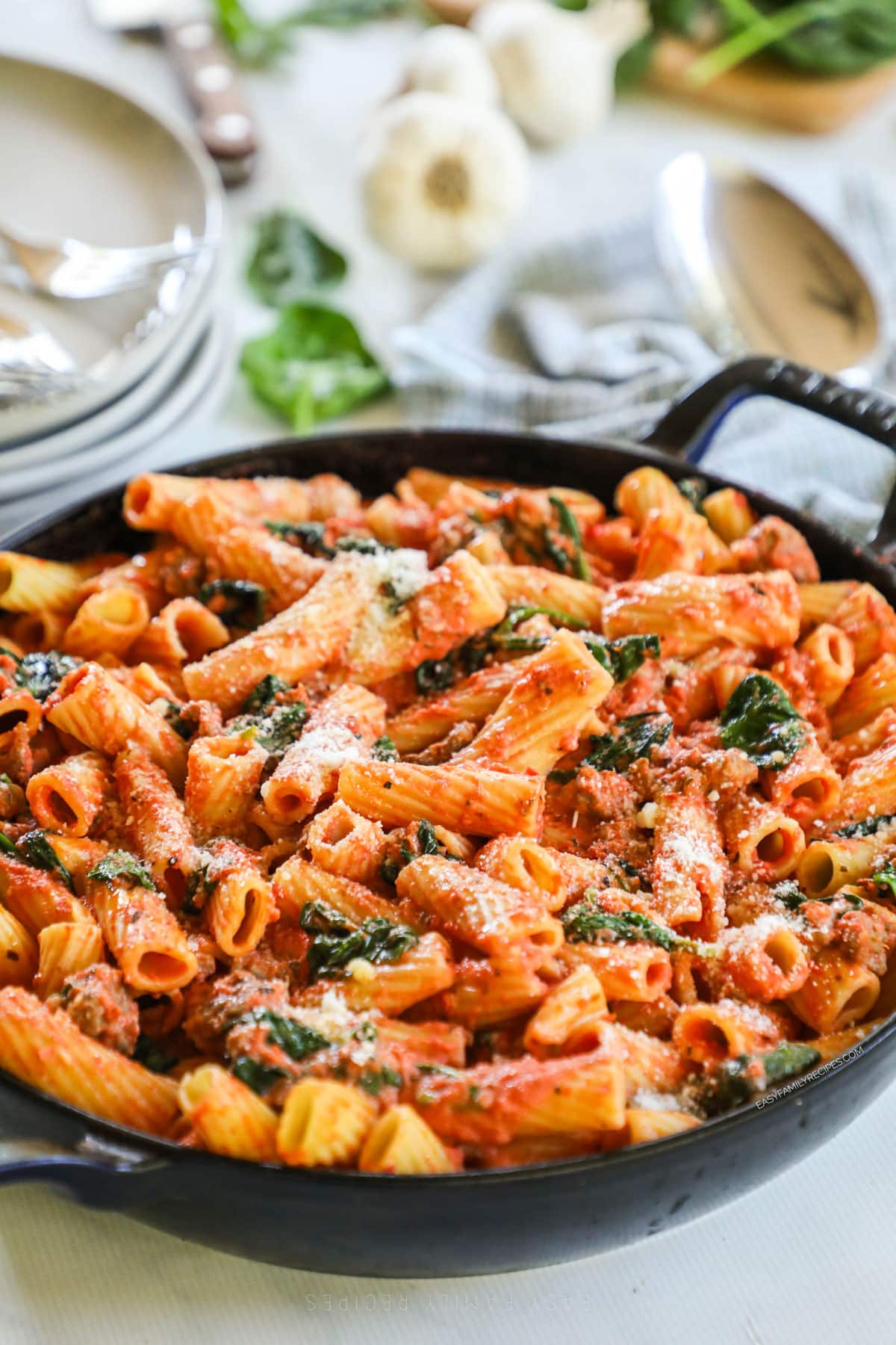 A large black pan full of creamy Tuscan sausage pasta with wilted spinach.