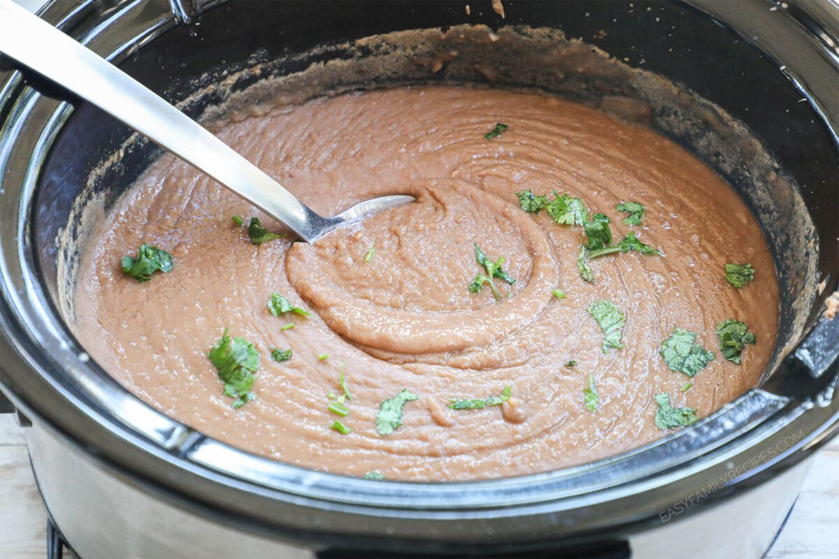 Mexican Refried Beans in a crockpot with a spoon
